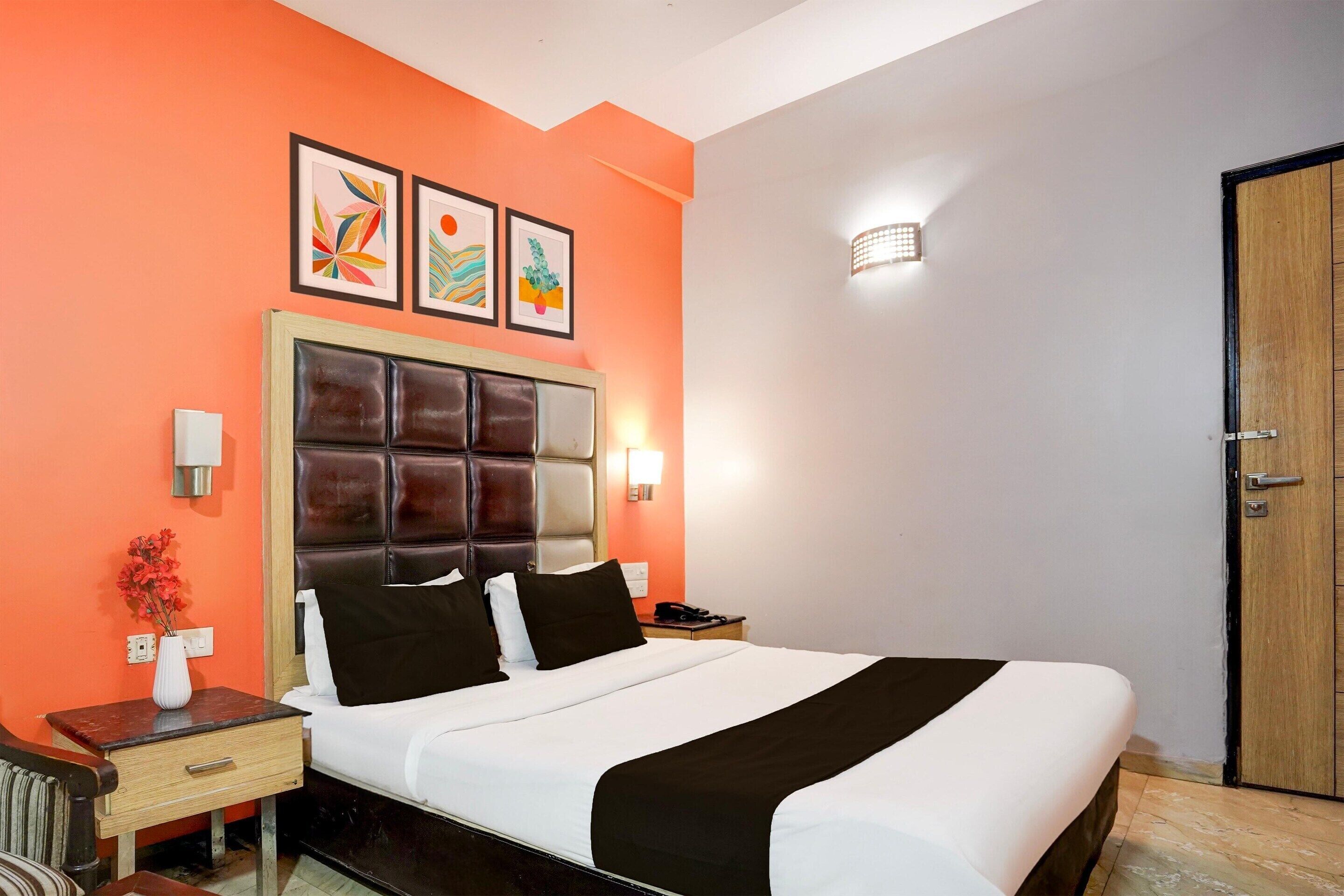 A hotel room with a large bed, a nightstand with a lamp, a vase with flowers, and artwork on the wall.