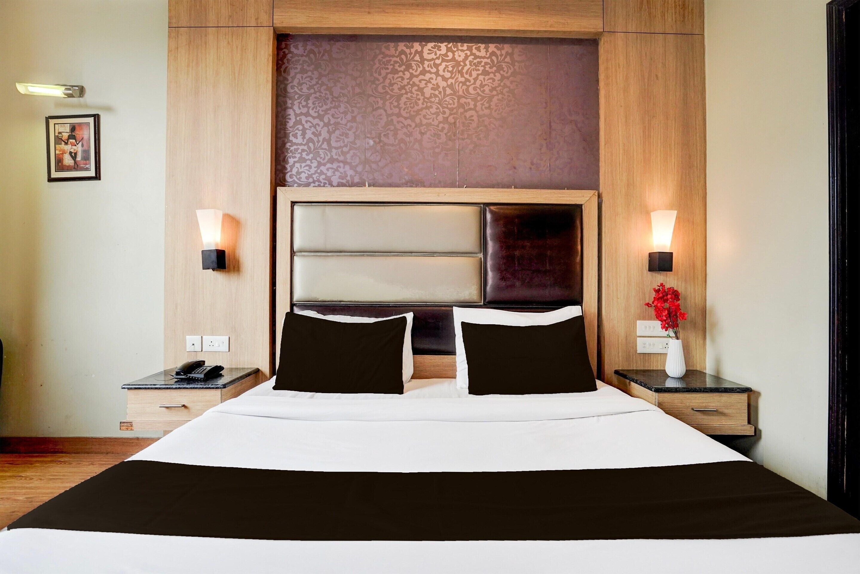 A hotel room with a large bed, two bedside tables, a nightstand, a wall-mounted lamp, and a framed picture on the wall.