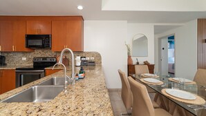 A modern kitchen with granite countertops, stainless steel appliances, and a dining area with a glass table and chairs.