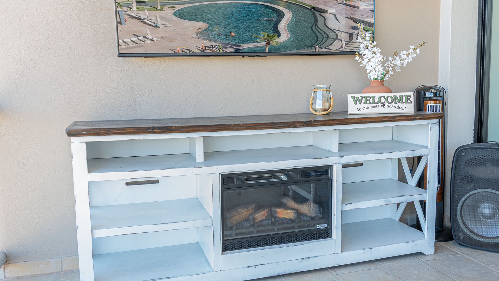 A white wooden console table with a 'WELCOME' sign, a vase with white flowers, and a speaker.