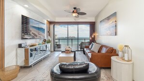 A modern living room with a leather sofa, a coffee table, and a large window overlooking the sea.