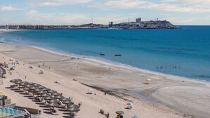 A beach with umbrellas, sun loungers, and a view of the ocean and distant buildings.