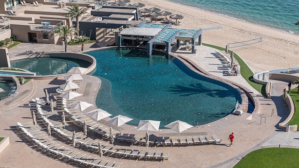 An aerial view of a resort with a large central pool, sun loungers, and a beach area.