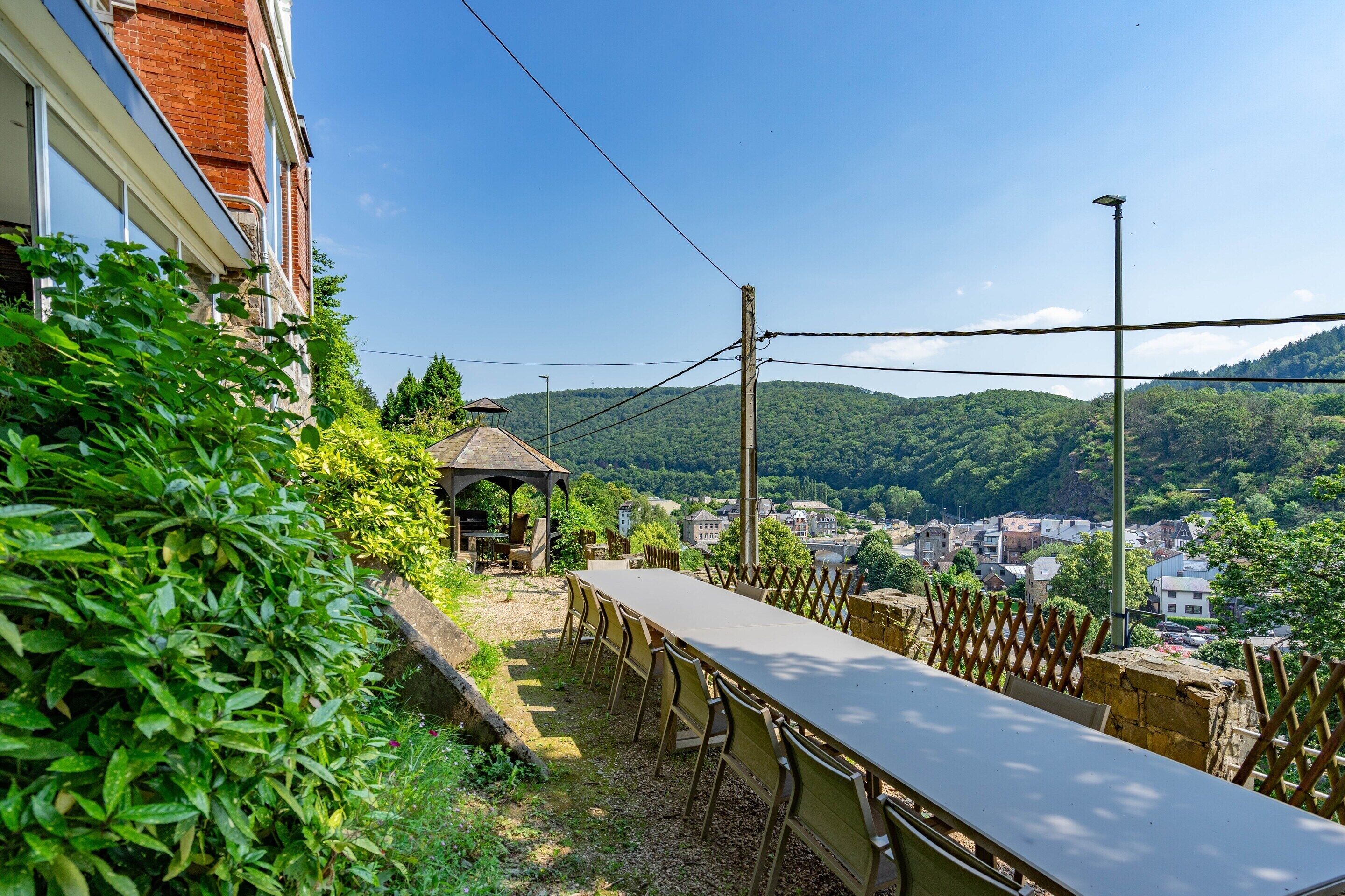 A long table with chairs, a gazebo, and a view of a town and hills.