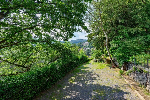 A gravel path flanked by dense green foliage, leading to a stone wall and a building in the distance. - Elegant Castle for 12 Guests (La Roche-en-Ardenne)
