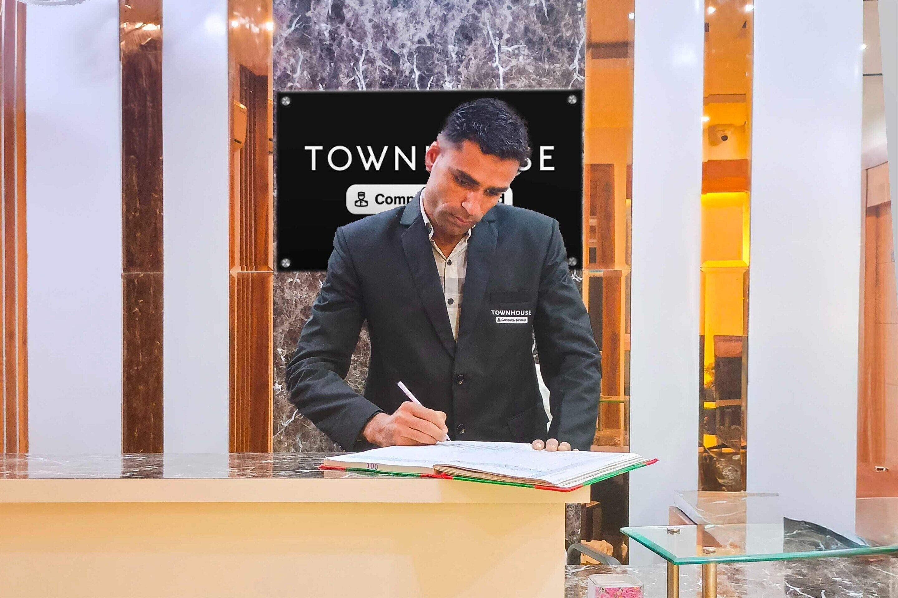 A man signing a document at a reception desk with a 'Townhouse' sign in the background.