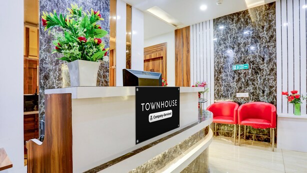 En receptionsdisk med en skylt som visar texten ”TOWNHOUSE – företagstjänster”, en krukväxt och röda stolar.