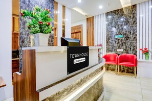 A reception desk with a sign reading 'TOWNHOUSE Company Serviced,' a potted plant, and red chairs. - Classic With Balcony Model Town Rohtak (Rohtak)