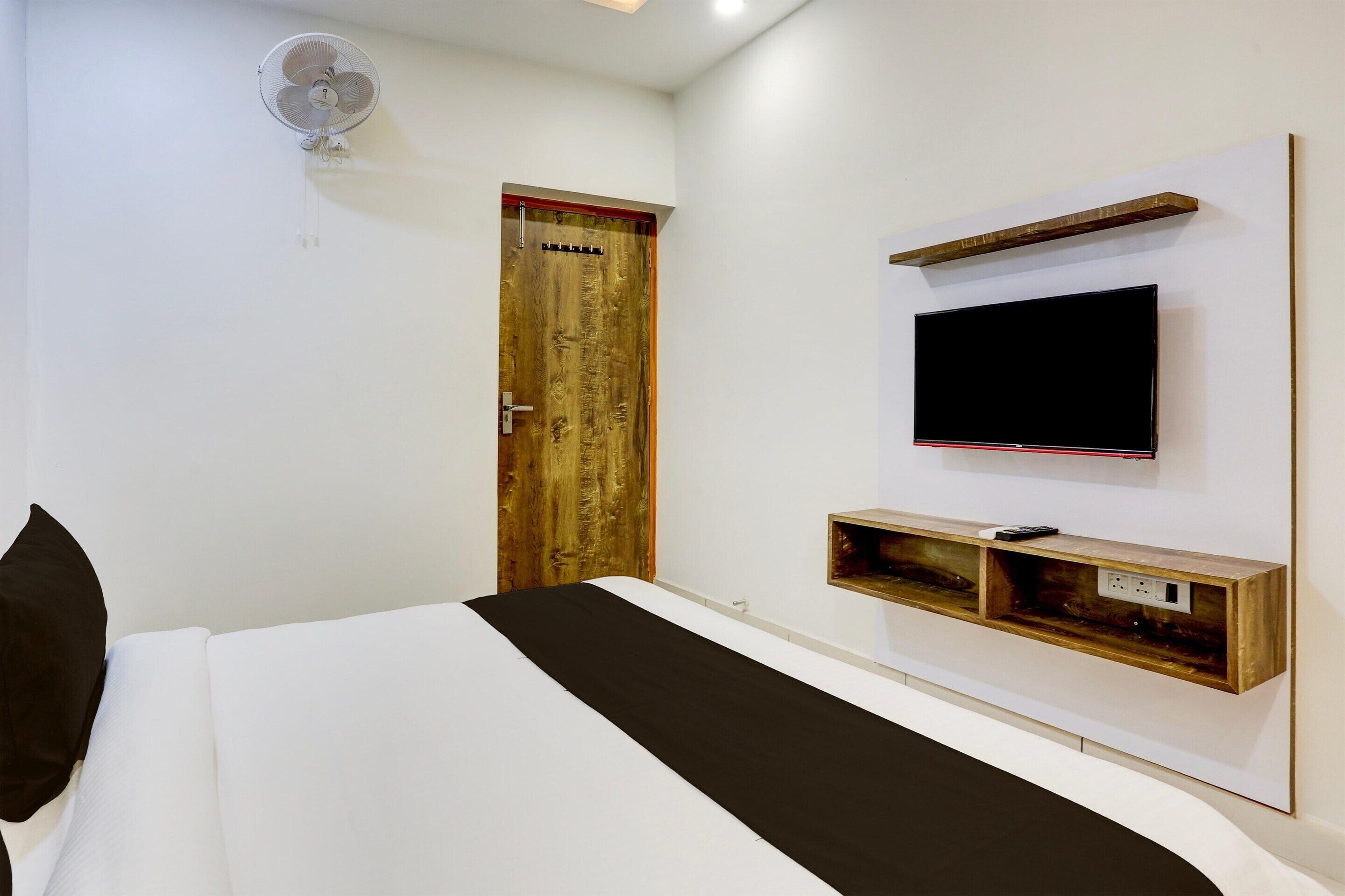 Un dormitorio con cama, una puerta de madera, un televisor montado y un estante fijado a la pared.
