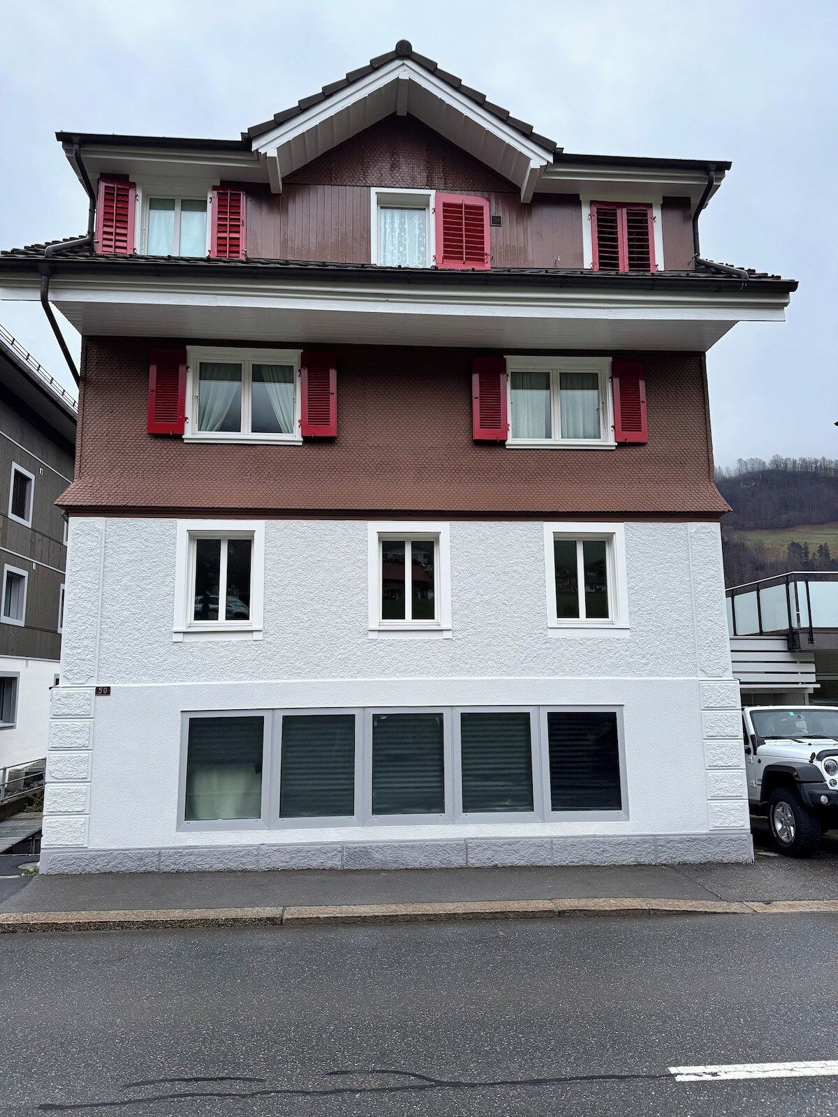 A multi-story residential building with a symmetrical facade, red shutters, and a white lower section.