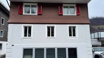 A multi-story residential building with a symmetrical facade, red shutters, and a white lower section.