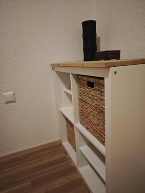 Ein Teil eines Raumes mit weißer Wand, Holzboden und einer weißen Regaleinheit mit einem gewebten Korb.