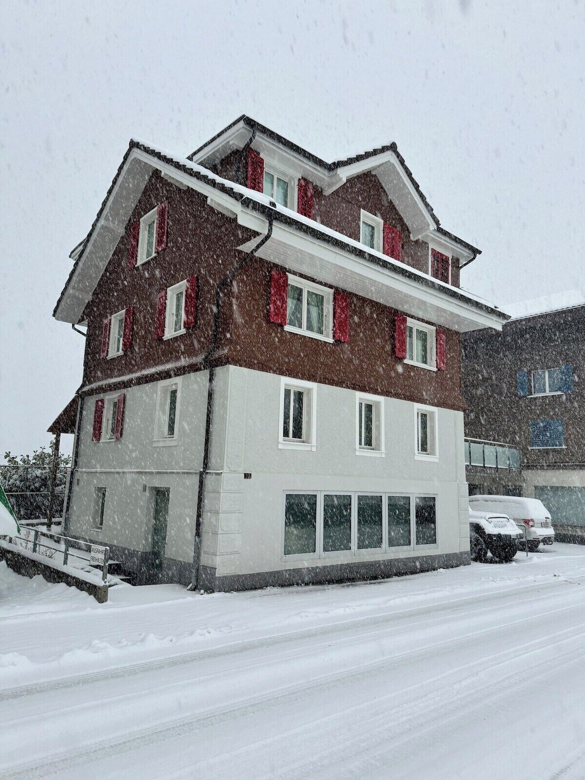 Ein mehrstöckiges Gebäude mit verschneiter Fassade, einer sichtbaren Garage und einem geparkten Auto.