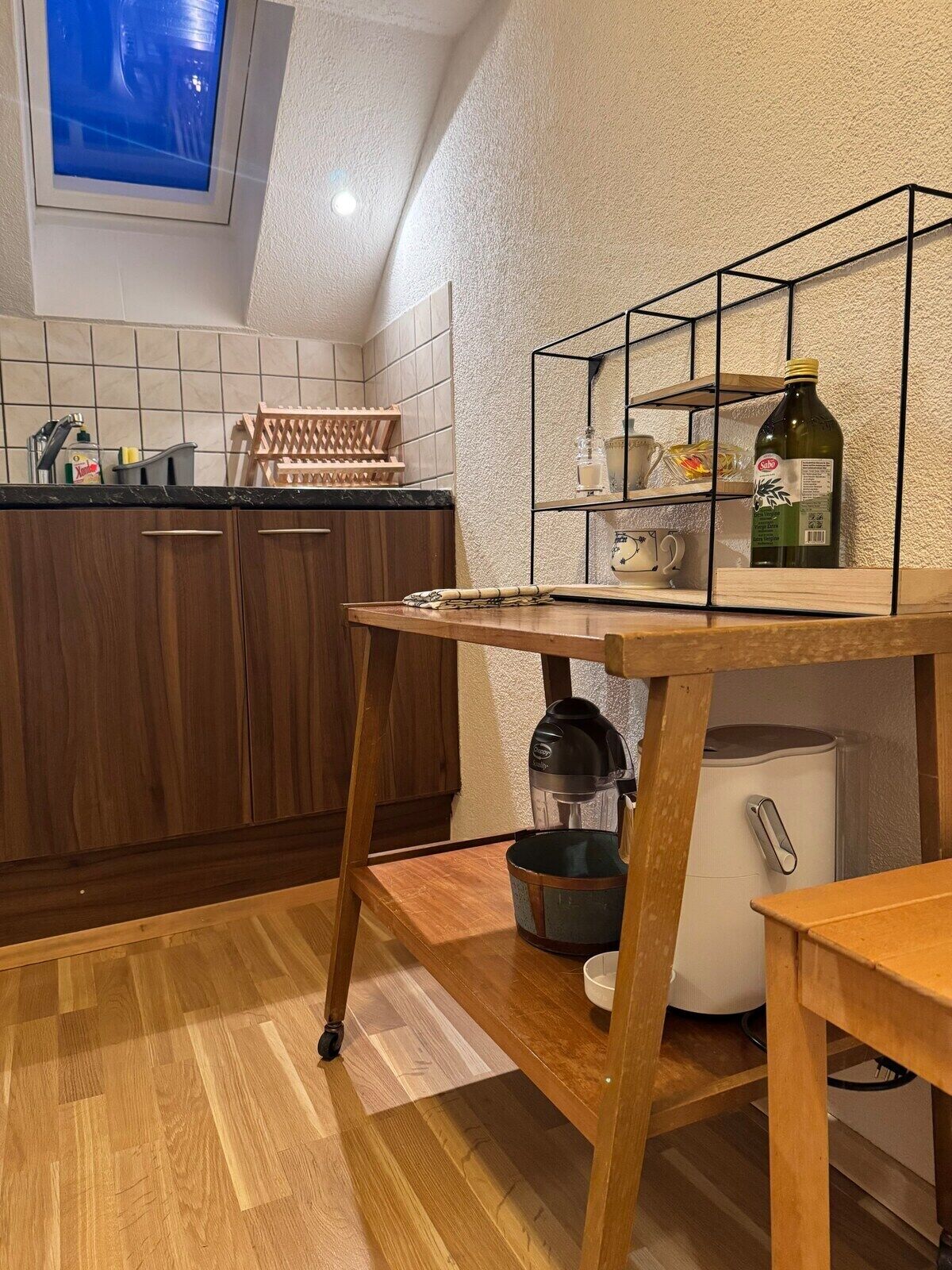 Une cuisine avec des meubles de rangement en bois, un plan de travail, une étagère intégrée, une machine à café et un réfrigérateur.