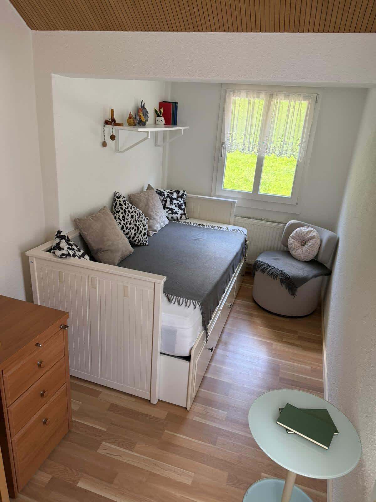Une chambre à coucher avec un lit, une table de chevet et une petite table ronde sur laquelle sont posés des livres.