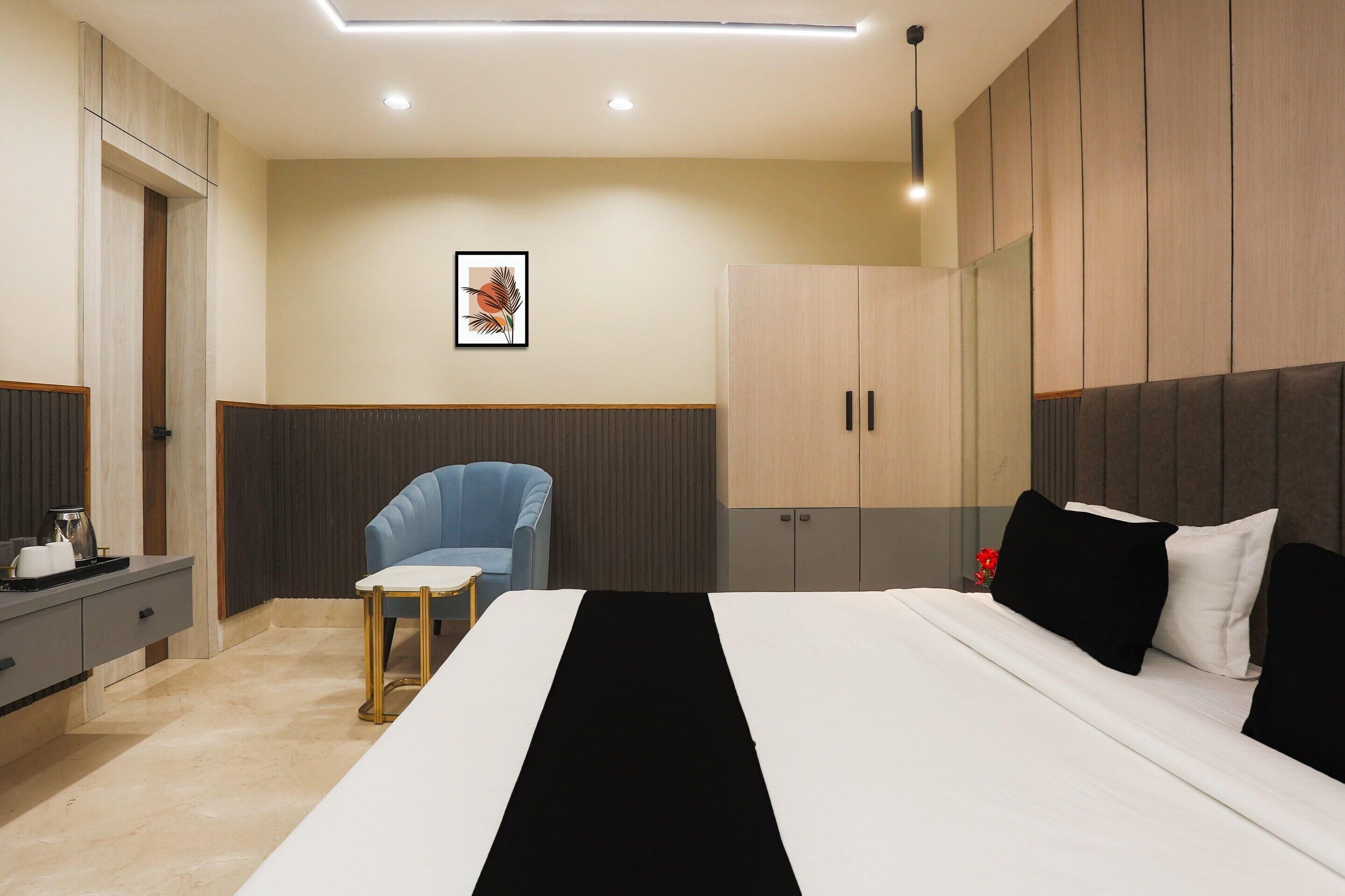 Ett modernt hotellrum med en säng, ett sängbord, en stol, en garderob och en inramad tavla på väggen.