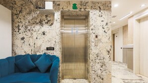 An elevator with a marble wall, a blue sofa, and a table in a hallway. - Deluxe Hotel Heritage Plaza (Hisar)