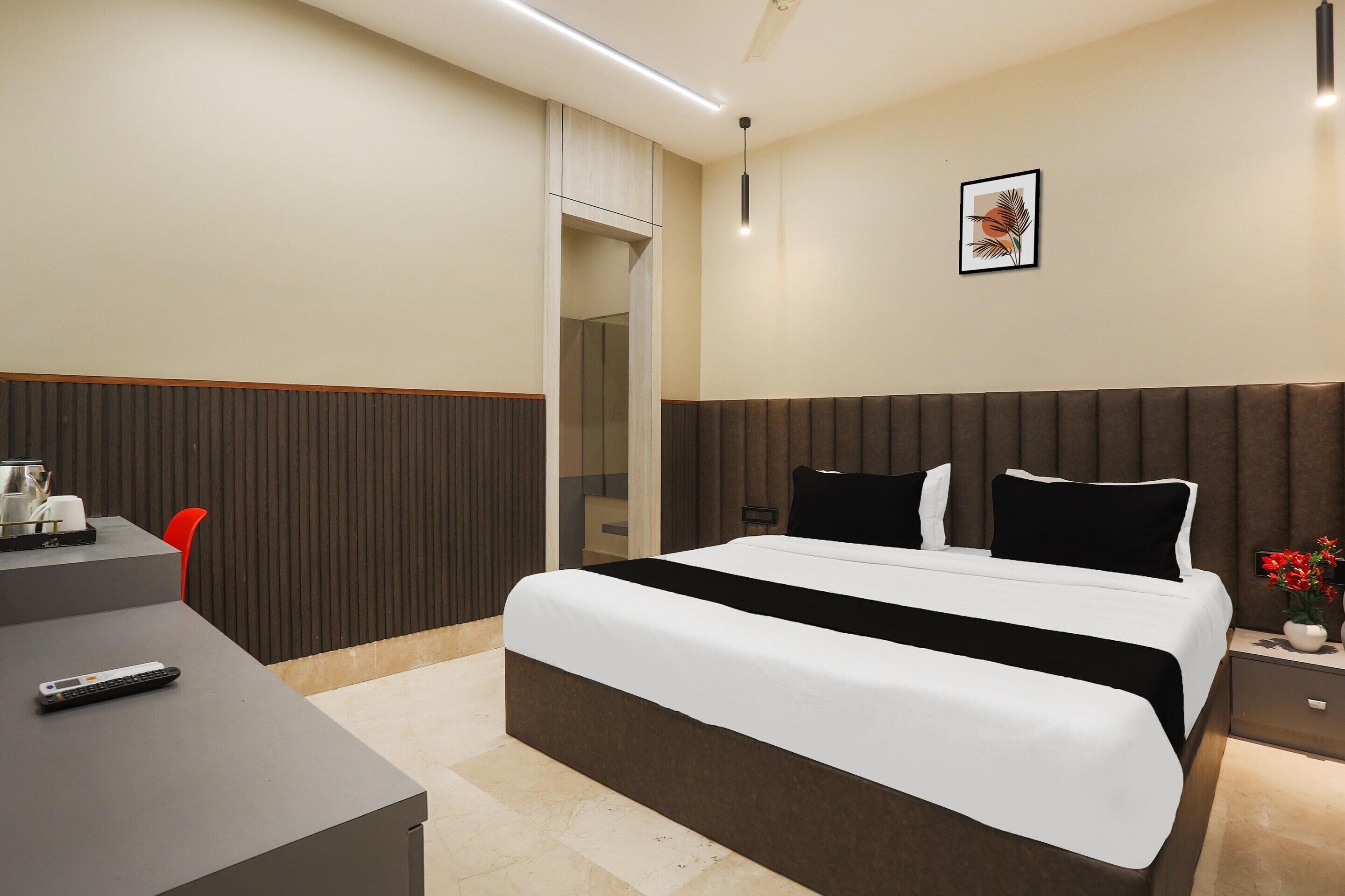 A hotel room with a bed, bedside table, and a desk with a remote control.