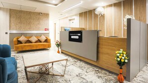 A reception area with a reception desk, a sofa, a coffee table, and a vase with flowers. - Deluxe Hotel Heritage Plaza (Hisar)