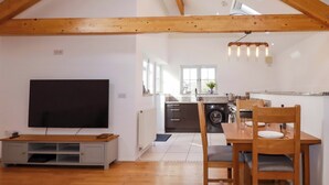 Ein geräumiger Loft mit hoher Decke, Holzbalken, einer Küche mit Waschmaschine und einem Essbereich mit Tisch und Stühlen.