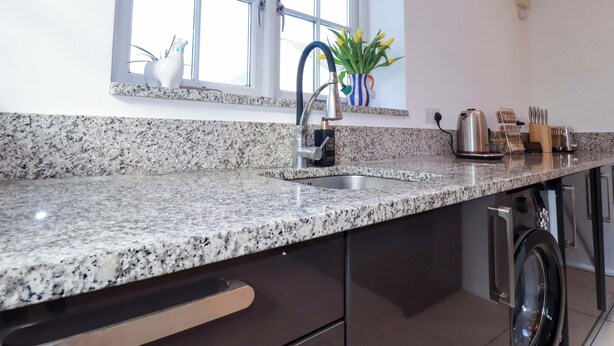 Eine Küche mit Granit Arbeitsplatten, einer Edelstahl-Spüle, einem Fenster und einem Geschirrspüler.