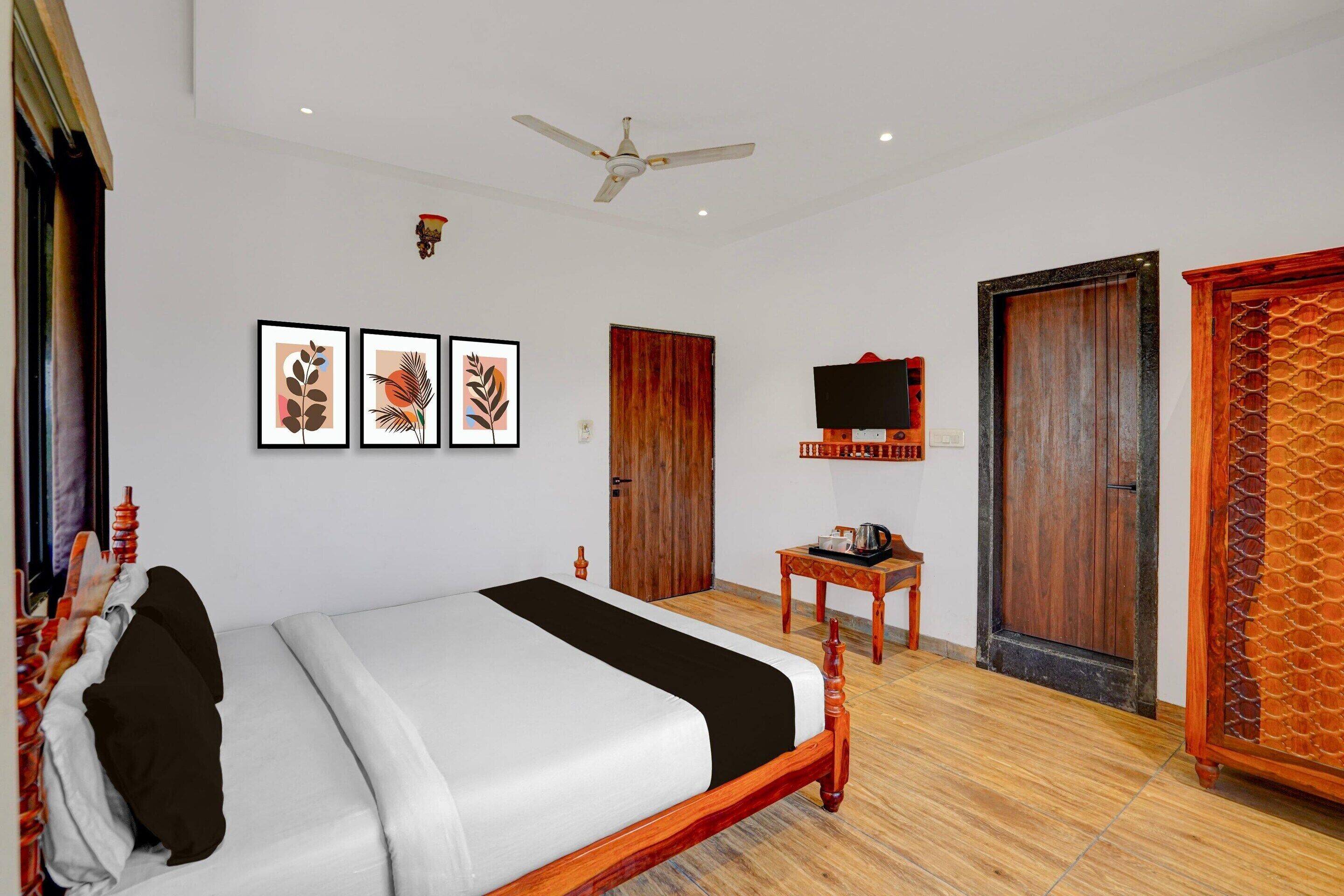 Quarto de hotel com cama, ventoinha no teto, televisão e portas de madeira.
