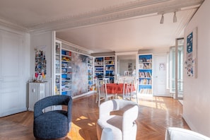 Ein geräumiges Wohnzimmer mit einer großen Bücherwand, einem Essbereich und Blick ins Freie.