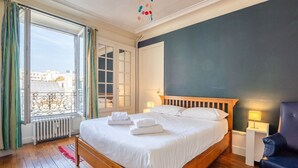Een slaapkamer met een houten bed, uitzicht op de stad door een raam en een balkon met een hekwerk.