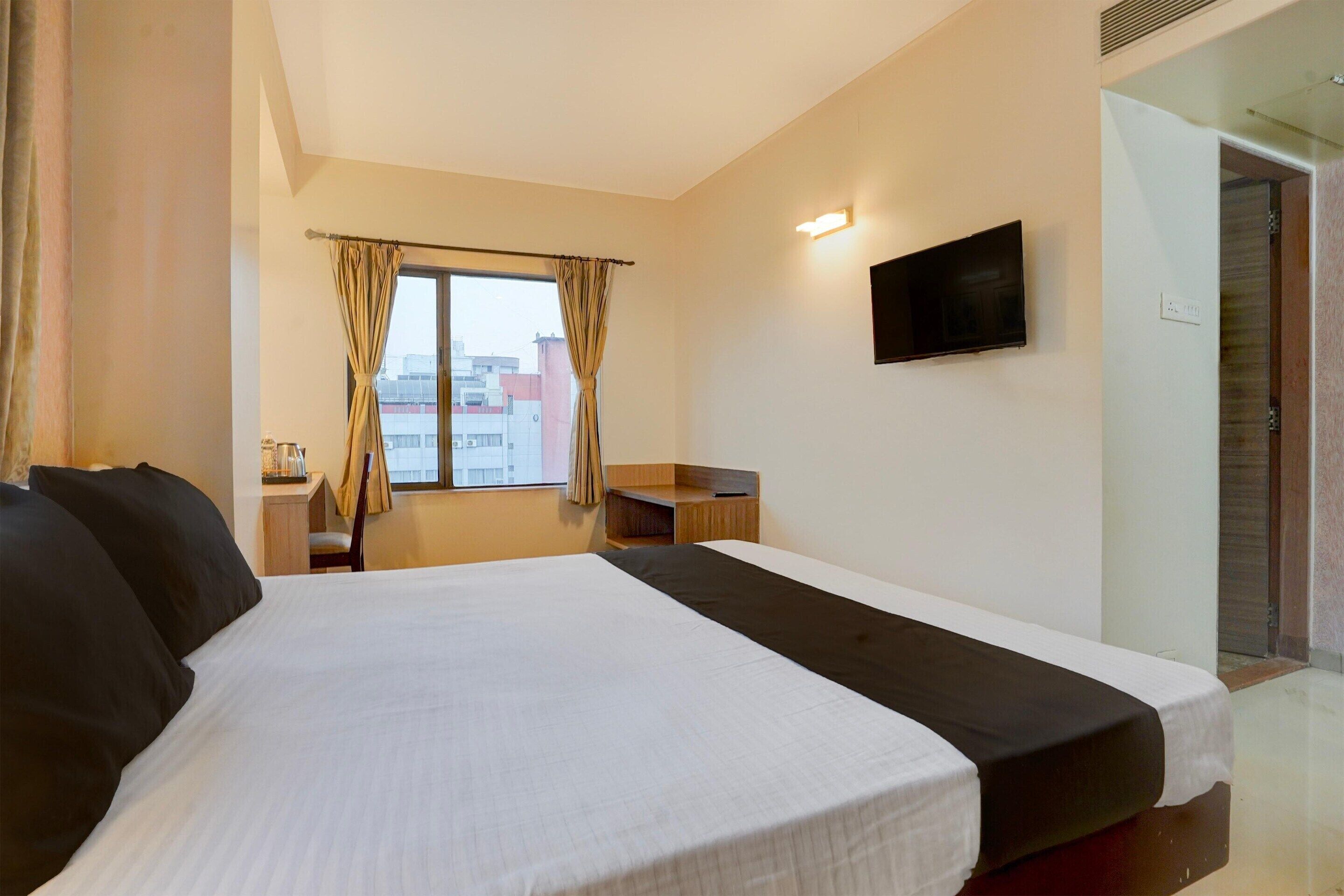 Habitació d'hotel amb un llit gran, una televisió, un escriptori i una finestra amb cortines.