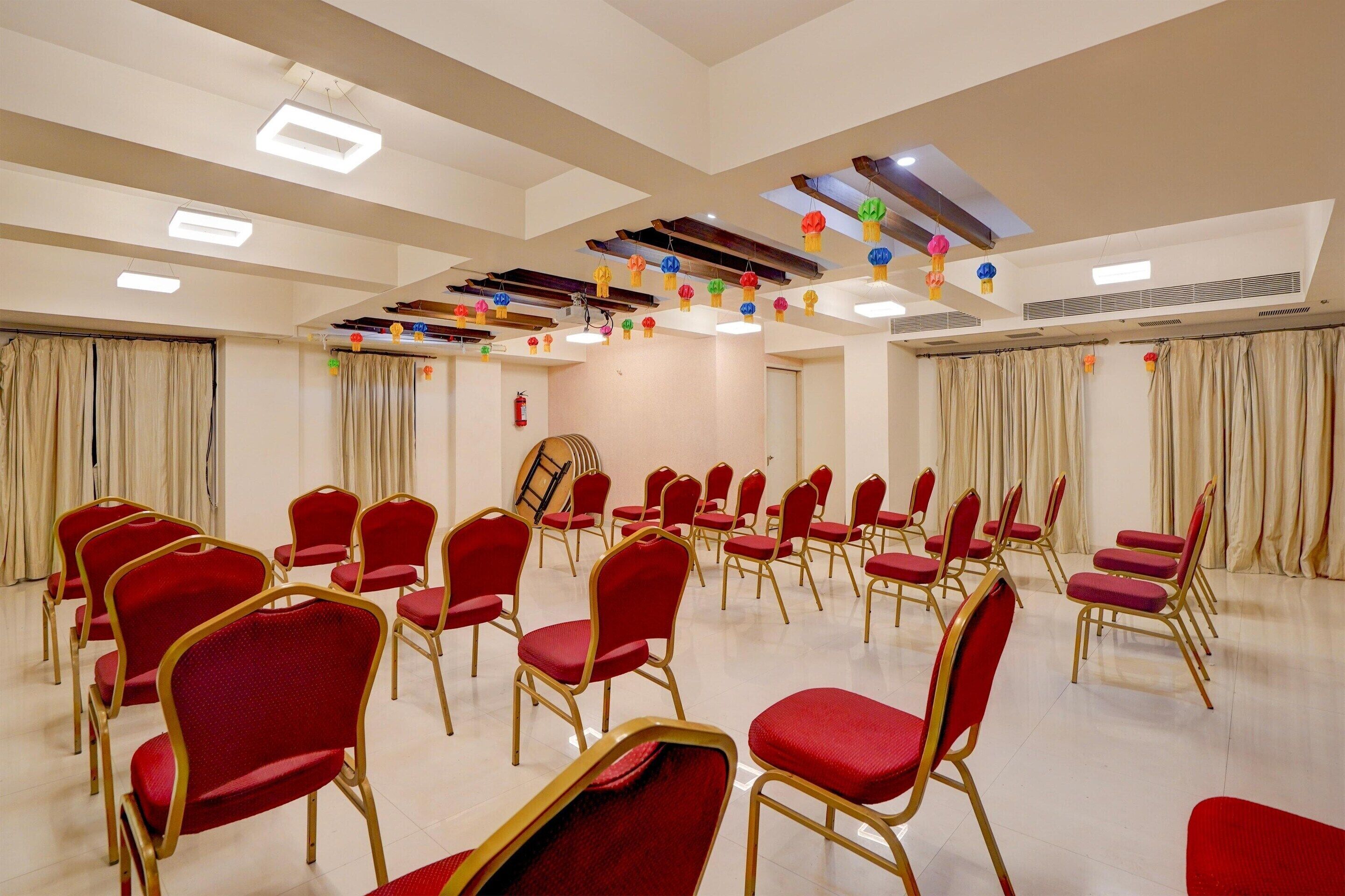 Une salle de conférence avec des rangées de chaises rouges, une scène en bois et des luminaires au plafond.