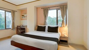 A hotel room with a large bed, a desk, a chair, and a window with curtains. - Deluxe Hotel Kapil Residency (Pune)