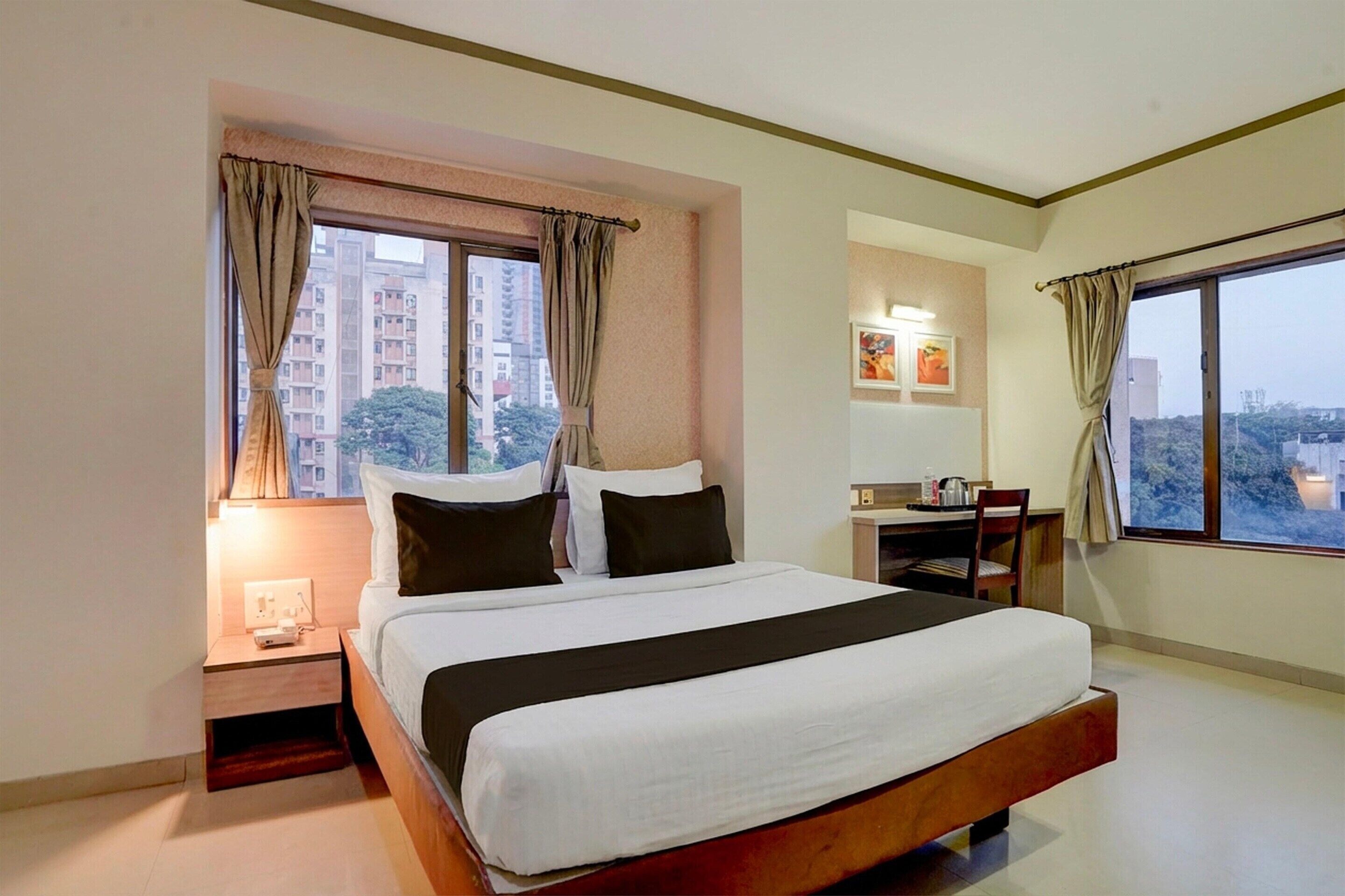A hotel room with a bed, a desk, a chair, a nightstand, and a window with curtains.