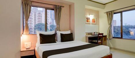 A hotel room with a bed, a desk, a chair, a nightstand, and a window with curtains.