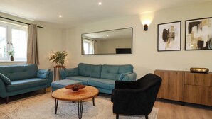 Una sala de estar con un sofá, una mesa de centro, un sillón negro, un aparador de madera y un espejo grande.