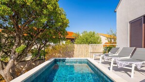 A rectangular swimming pool with clear blue water, surrounded by a wooden fence, and adjacent to a building with a white exterior. - Villa Mila Near Beaches & Center (Supetar)