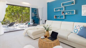 A modern living room with a white sofa, a laptop on a round wicker side table, and a view of a balcony with outdoor furniture. - Villa Mila Near Beaches & Center (Supetar)