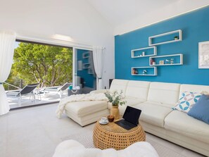 A modern living room with a white sofa, a laptop on a round wicker side table, and a view of a balcony with outdoor furniture. - Villa Mila Near Beaches & Center (Supetar)
