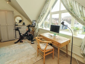 Ein Schlafzimmer mit Schreibtisch, Stuhl, Hometrainer und einem großen Fenster mit Vorhängen.