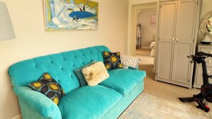 A teal sofa with patterned cushions, a painting above it, and a closed wardrobe in the background. - Lakes View (Keswick)
