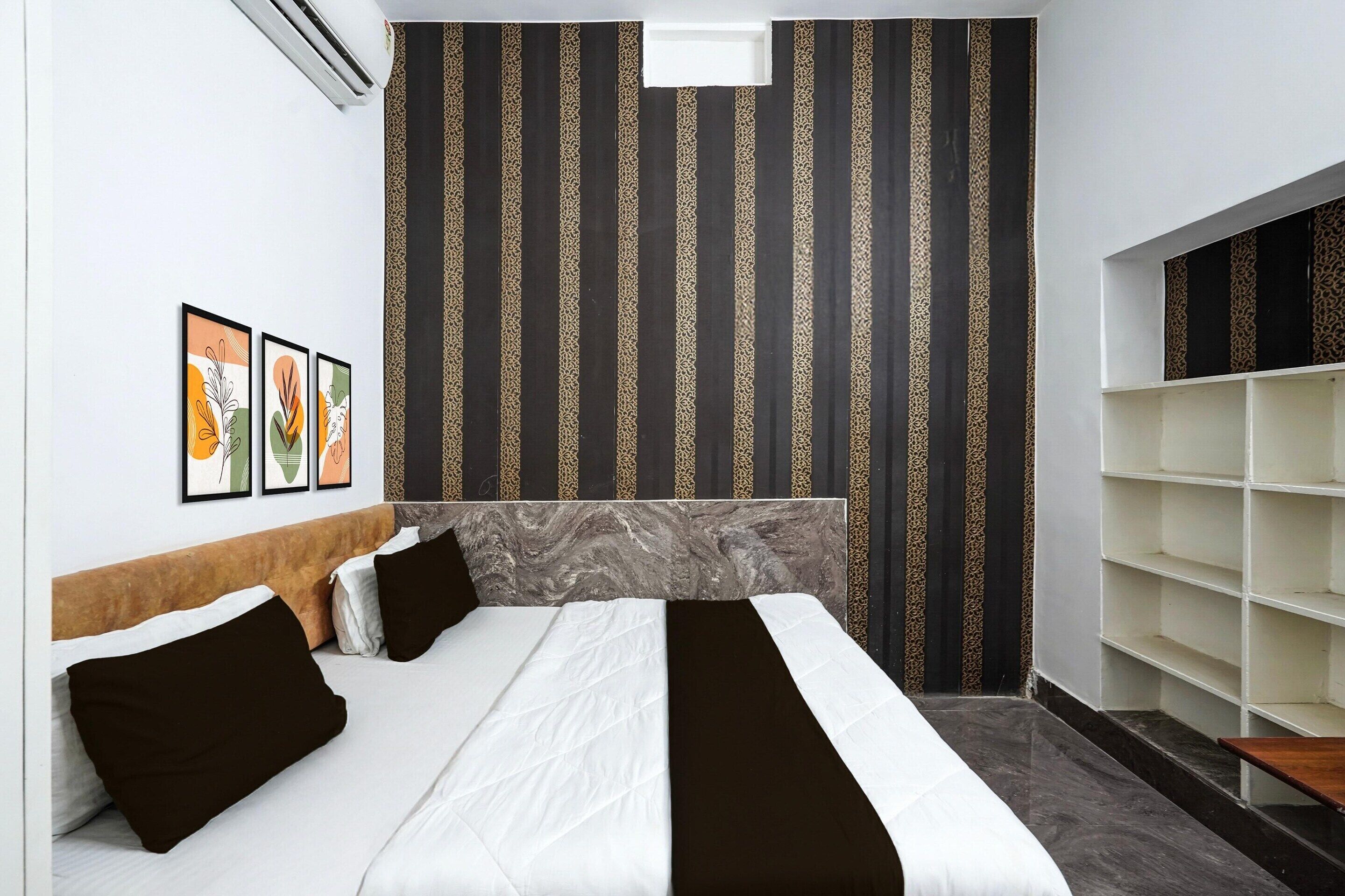 A hotel room with a bed, a headboard, a wall with vertical stripes, and a shelf unit.