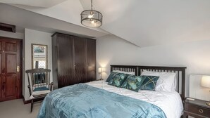A bedroom with a large bed, dark wooden wardrobe, a chair, and a hanging light fixture. - Preswylfa (Cemaes Bay)