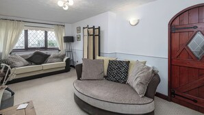 A living room with a curved sofa, a wooden door, and a window with curtains. - Preswylfa (Cemaes Bay)