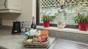 A kitchen counter with a coffee maker, wine glasses, a basket of eggs, and potted plants by a window. - Preswylfa (Cemaes Bay)