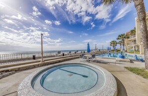 Un espace piscine offrant une vue sur l’océan, avec un palmier et un bâtiment doté de balcons.