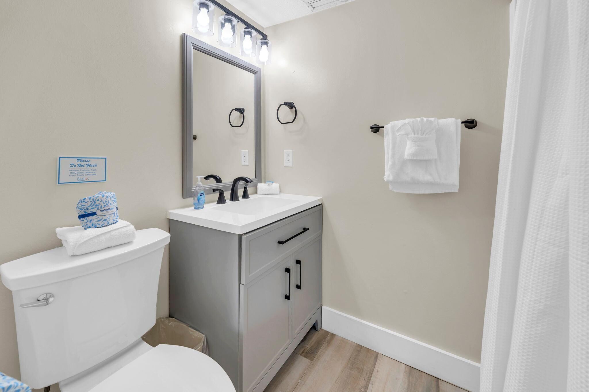 A bathroom with a toilet, sink, mirror, towel rack, and a sign on the wall.