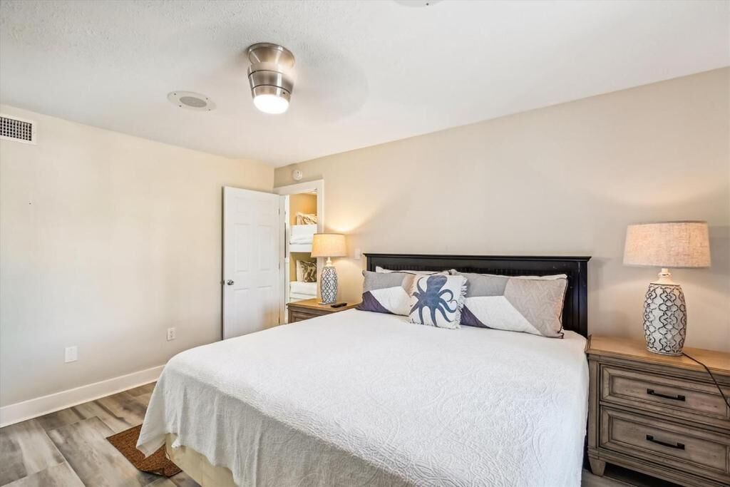 Un dormitorio con cama, mesitas de noche, lámpara y puerta que da a un baño.