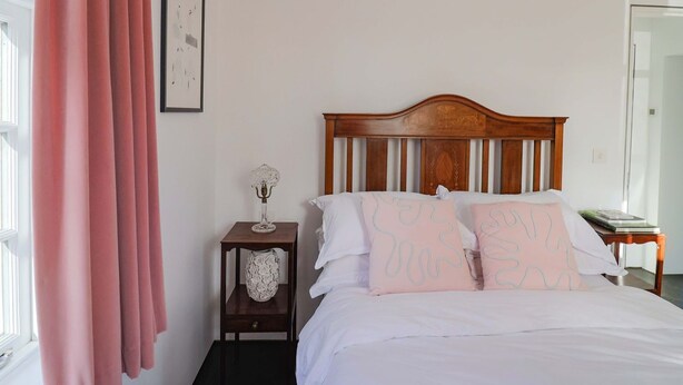 Una camera da letto con una testiera in legno, biancheria da letto bianca, un comodino con un vaso e un quadro appeso al muro.