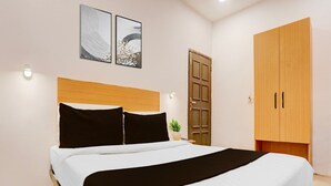 A bedroom with a bed, a wooden wardrobe, and two wall-mounted artworks. - Deluxehotel Woodland (Nagpur)
