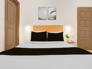 A bed with a wooden headboard, two black pillows, a white bedspread, and a small bedside table with a plant.