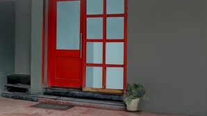 A red door with glass panels, a potted plant, and a small step leading to the entrance. - Deluxehotel Woodland (Nagpur)